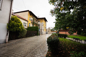 A quiet Tarnow street scene with yellow buildings, cobblestone road, and park benches in Poland