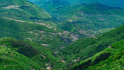 Fototapeta premium An aerial perspective of a mountain valley filled with green forests and scattered villages surrounded by hills, roads, and nature.