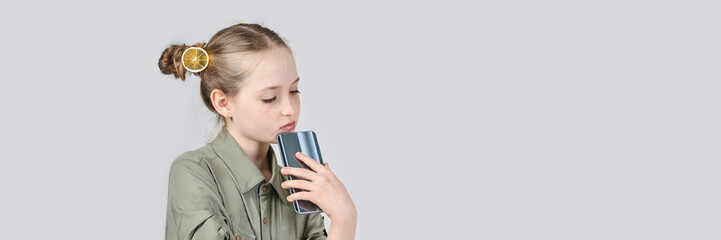 Young caucasian girl with lemon hair accessory holding smartphone on grey background.