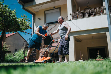 Two men work together in a bright yard, guiding a lawn mower as they maintain the grass in front of a house, highlighting outdoor activity and teamwork on a sunny day.