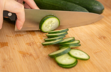 Slicing cucumbers with a large knife on wood cooking board close-up