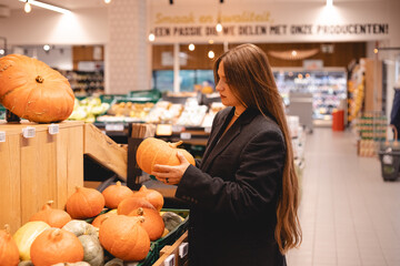 Unrecognizable girl choosing pumpkin in supermarket near shelf with organic fruits and vegetables....