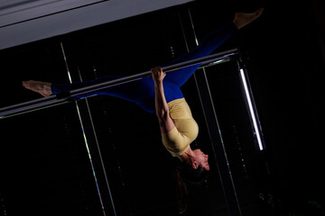 Pole dancer performs an impressive inverted pose during an indoor training session in a brightly lit studio late in the evening