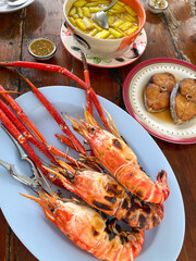 Grilled river prawns with dipping sauce and side dishes on wooden table, savory and vibrant seafood meal