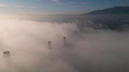 Aerial drone view of a tall orange and white industrial smokestack emerging from thick fog, with peeling paint, maintenance ladders, and a hazy pastel sky creating an atmospheric scene of aging infras - Powered by Adobe