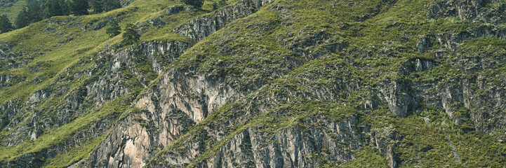 Scenic mountainside landscape with lush green vegetation and jagged rock formations at daylight.