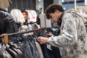 Teenage boy shopping for clothes in fashion store — young man browsing trendy outfits on rack, modern retail, teen lifestyle, casual fashion, youth shopping experience