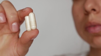 A woman holding two white capsules between her fingers. Taking vitamins, supporting the immune system, preventing the flu, and promoting a healthy lifestyle. A natural supplement or medicine in capsul