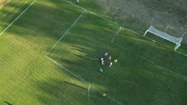 Drone aerial view of a football match in progress on a full size outdoor soccer field. Players, referee, and team formations are seen from directly above, capturing the strategy and movement of the ga