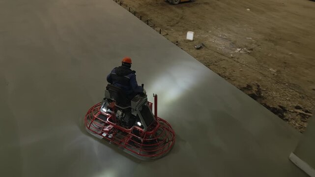 Construction worker using a ride on power trowel to finish concrete slab. Clip
