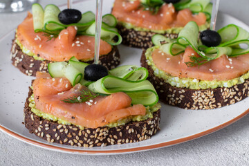 Sandwiches with salted salmon, black olives, avocado and cucumber on light gray background