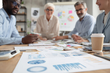 Fototapeta premium Office team engaged in discussion around a table with charts, documents and coffee cups