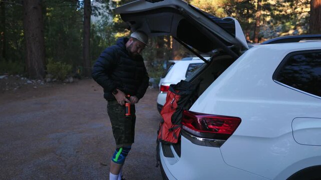 A man enthusiastically prepares for an exciting outdoor adventure, meticulously adjusting his gear at the back of an SUV, surrounded by the peaceful and serene forest environment