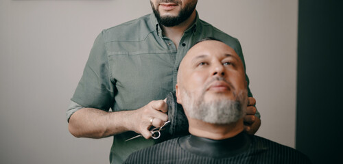 Male grooming session at barbershop with adult caucasian barber and mature male customer