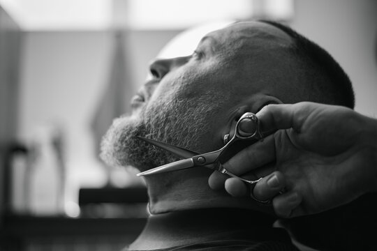 Caucasian male grooming at barbershop, precision beard trim by professional barber