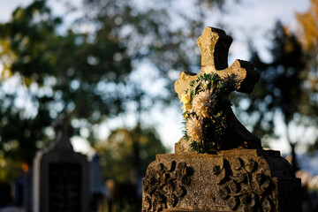 Stone cross adorned with flowers in a peaceful cemetery at sunset