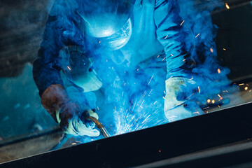 Skilled worker welding metal at shipyard with blue sparks in industrial setting