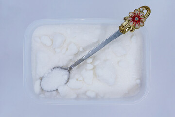 A plastic container filled with sugar with a small spoon