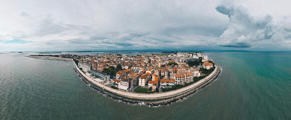 Grado, Italy with coastline, sea, and old town architecture under dramatic cloudy sky