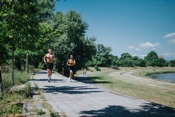 Fit people jogging on a sunny day in a green park beside a serene river. Promoting outdoor fitness, energy, and a healthy lifestyle in a picturesque natural environment.