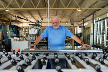 An elderly worker controls the process of installing glass in PVC frames.