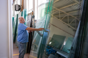 An elderly worker controls the process of installing glass in PVC frames.
