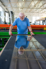 An elderly worker controls the process of installing glass in PVC frames.