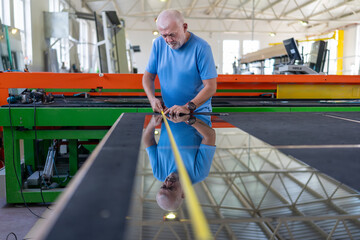 An elderly worker controls the process of installing glass in PVC frames.