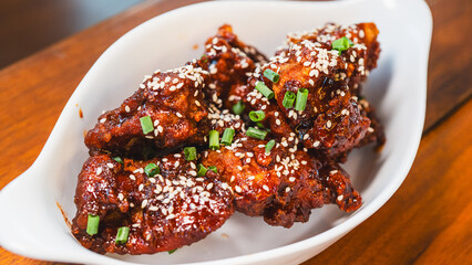 Sizzling, succulent Korean sticky chicken glistening with sauce, topped with sesame seeds and spring onions. A vibrant meal, beautifully presented in an elegant bowl within a stunning ambient setting.