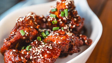 Sizzling, succulent Korean sticky chicken glistening with sauce, topped with sesame seeds and spring onions. A vibrant meal, beautifully presented in an elegant bowl within a stunning ambient setting.