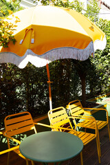 A cozy lounge area in a cafe on an open veranda with yellow chairs and a table. Lush green plants...