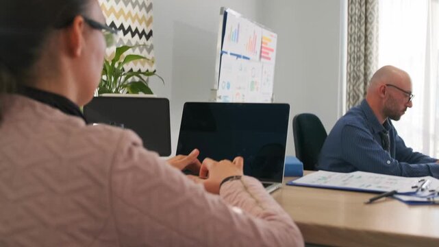 organized woman working, calm woman preparing presentation materials, white woman efficiently organizing meeting documents at desk, professional woman working on laptop amidst planners and conference