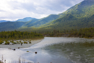 A serene river flows through a valley surrounded by mountains, the Altai mountain landscape is...