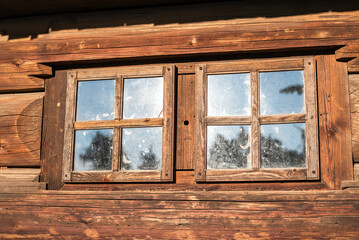 Old wooden windows with glass panes on a rustic log cabin wall in sunlight. Vintage wooden framed window on an old log house