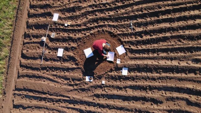 Soil scientist examining ground samples, surrounded by research equipment in expansive agricultural landscape during field investigation