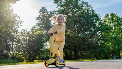 Toddler on scooter. Yellow scooter ride girl. Child park activity summer.