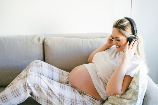 Young happy pregnant woman listening to music for baby in headphones. Motherhood.