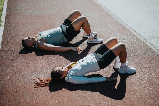 A muscular and sporty couple engaging in fitness training outdoors on asphalt, promoting teamwork, outdoor activity, and a healthy lifestyle.