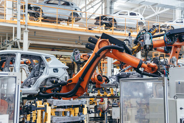 Multiple orange robotic arms welding and working on steel car bodies suspended on elevated platforms