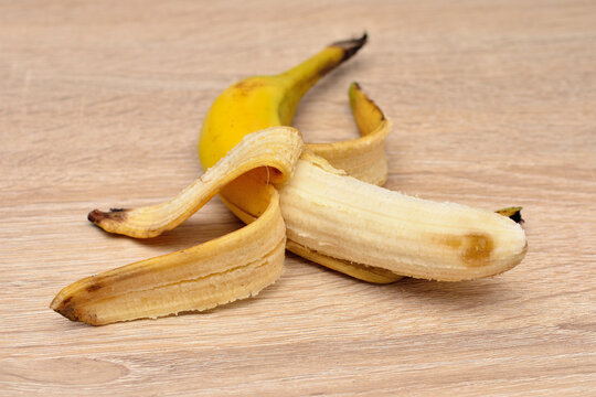 A peeled yellow banana with its skin on a wooden table