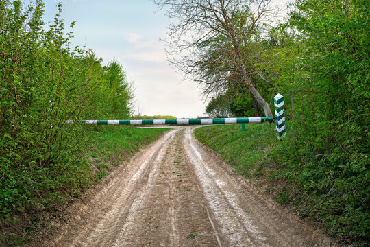 Dirt road leading into a forest blocked by a green and white barrier