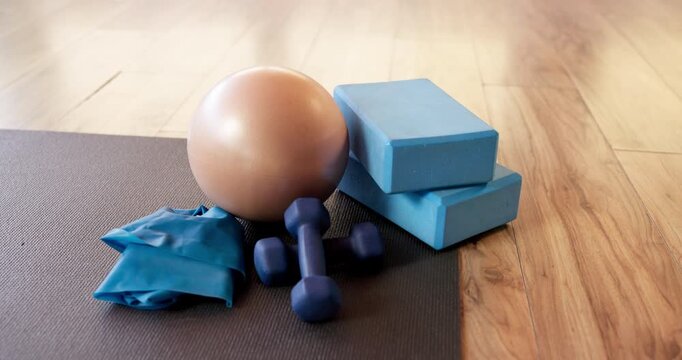 Yoga, equipment and dumbbells with mat in studio for fitness, workout or health routine. Empty room, stability ball or resistance band with weights for exercise, pilates or physical activity on floor