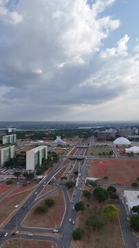 Vis&atilde;o a&eacute;rea de Bras&iacute;lia destacando avenidas, pr&eacute;dios e c&eacute;u nublado, revelando a organiza&ccedil;&atilde;o urbana e a arquitetura moderna da capital federal em um registro amplo