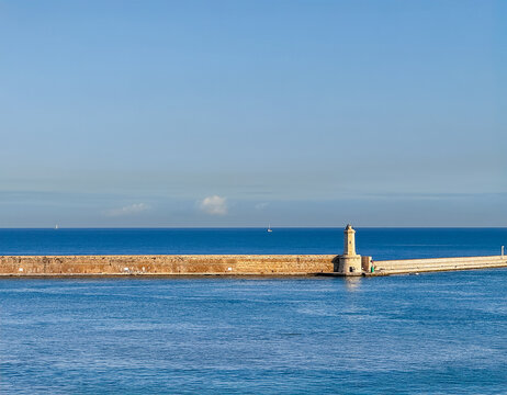 Livorno, Italy, Europe - July 14, 2024: Breakwater dam in front of harbor with short light beacon in middle. Blue sea water and sky