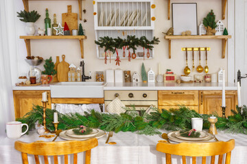 Elegant Christmas holiday table setting with greenery and simple decor on cozy kitchen background. Beautifully arranged holiday table with plates, candles and golden cultery on white tablecloth