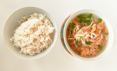 A bowl of rice and a bowl of soto kudus soup sit on a white table