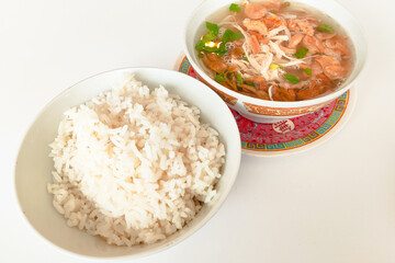A bowl of rice and a bowl of soto kudus soup sit on a white table