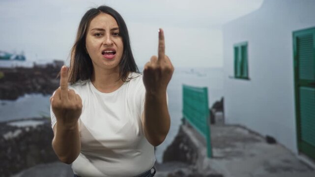 Woman showing middle finger with both hands on street by seaside promenade outdoors; defiance rebellion.