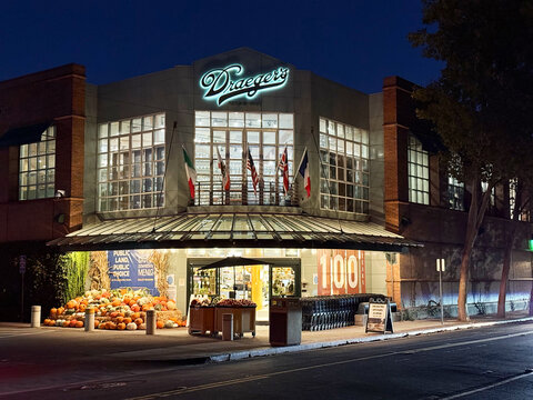 Exterior nighttime view of Draeger's Market grocery store building with seasonal pumpkin display, glowing sign, and parked shopping carts - Menlo Park, California, USA - October 15, 2025