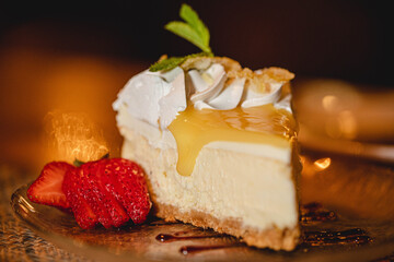 A slice of lemon cheesecake dessert with fresh strawberries and a mint garnish in a high end food restaurant 